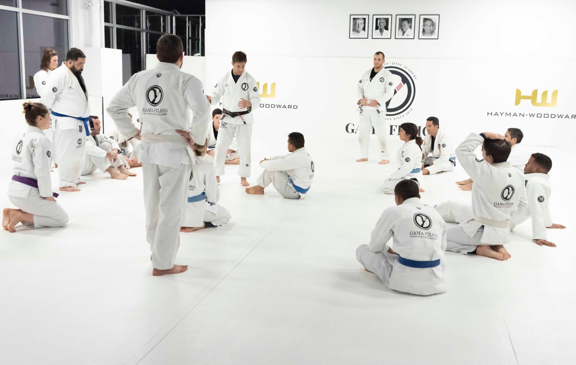 Adults Brazilian Jiu-Jitsu class gathered around the instructor on the academy mats